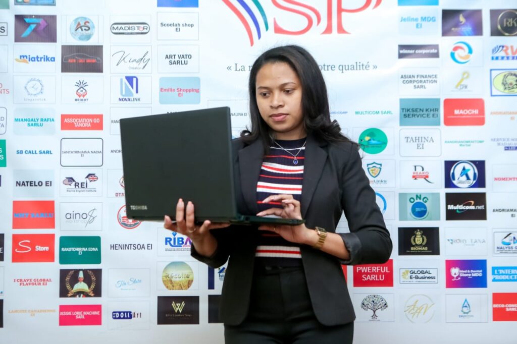 Une conseillère de Sitraka Prestataire consulte un dossier client sur son ordinateur portable, devant le mur des logos des entreprises accompagnées